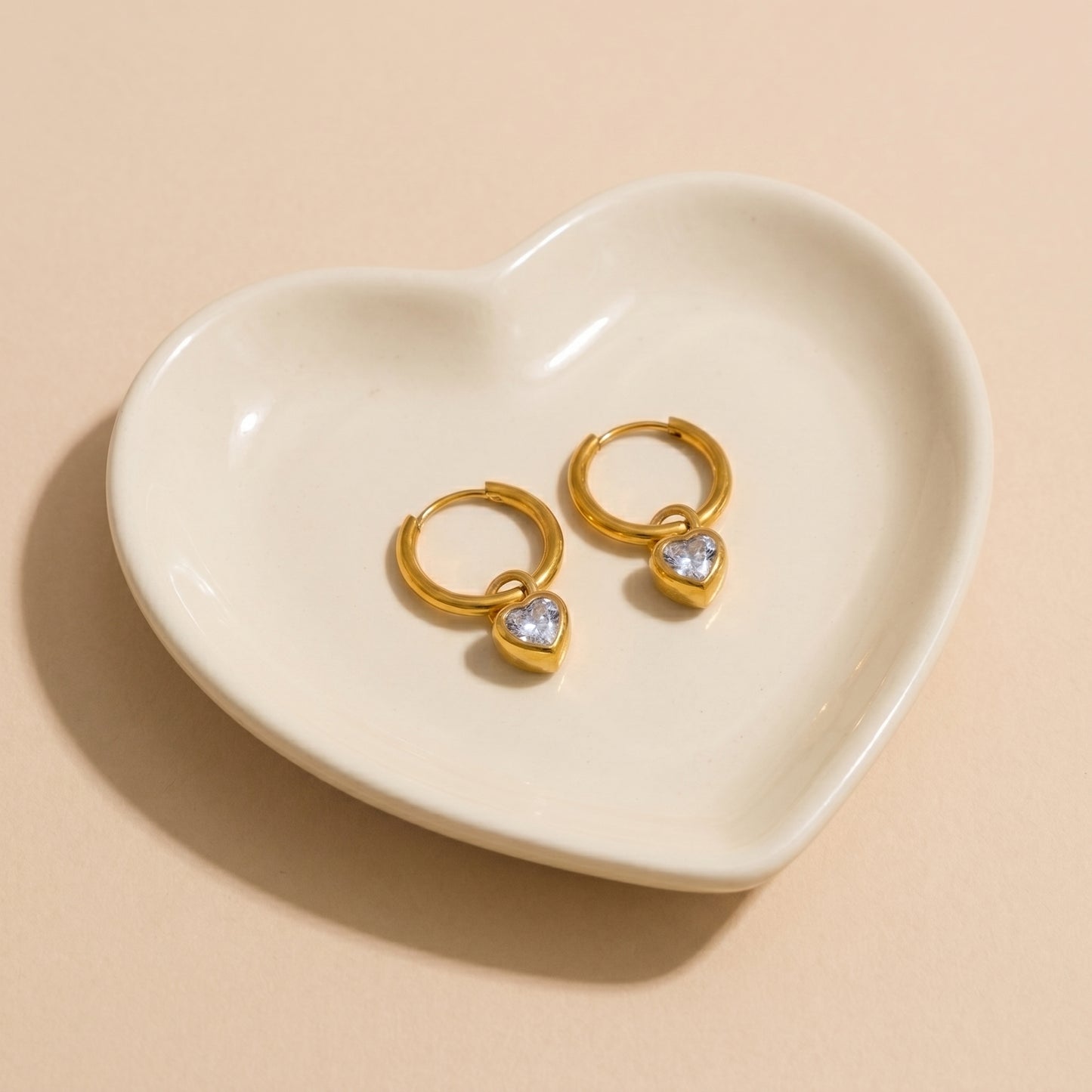 High quality waterproof gold plated huggie hoop earrings featuring sparkling clear crystal heart dangle charms, displayed on a clean background