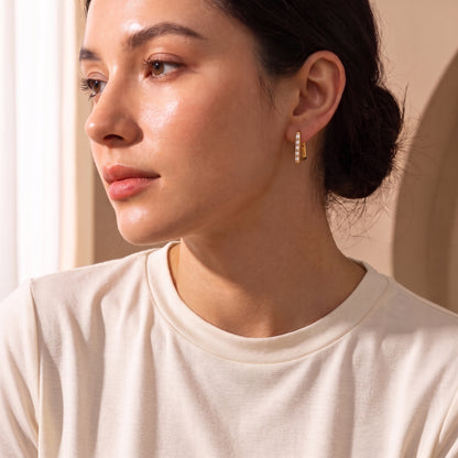 Close-up view of a woman's earlobe wearing the skin friendly Vendôme gold geometric baguette hoop earrings in natural studio lighting.