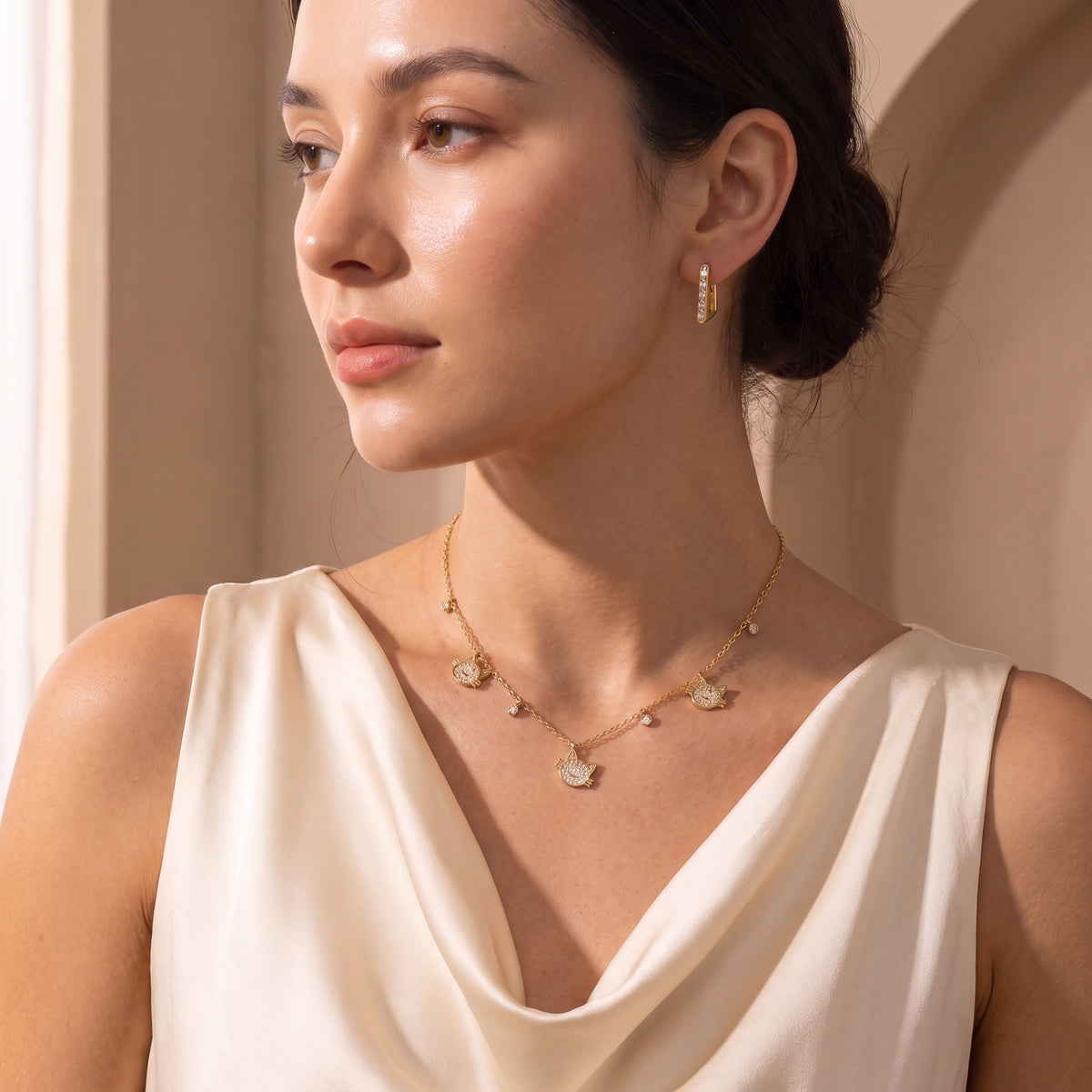 Editorial portrait of a woman wearing the waterproof Vendôme gold baguette geometric hoops paired with the Féline crystal cat necklace and a cream silk dress.