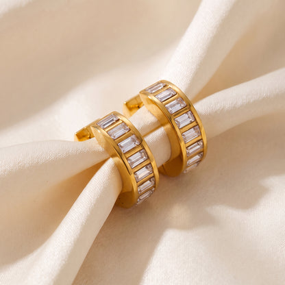 Tarnish-free Verona gold huggie earrings with rectangular clear crystals resting on draped champagne silk fabric.