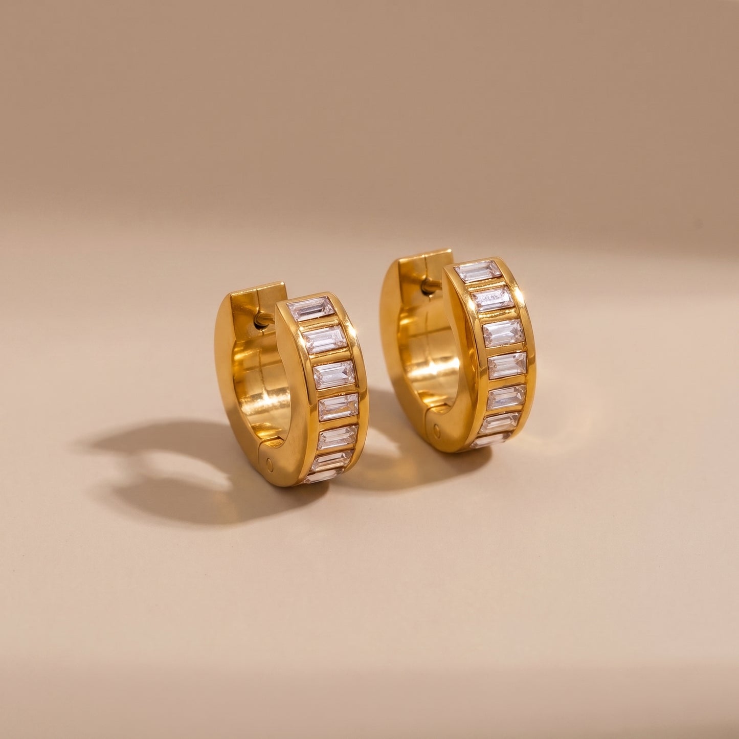 High quality Verona Gold Hoops featuring channel-set baguette crystals resting on a warm beige surface in natural sunlight.