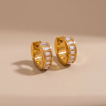 High quality Verona Gold Hoops featuring channel-set baguette crystals resting on a warm beige surface in natural sunlight.