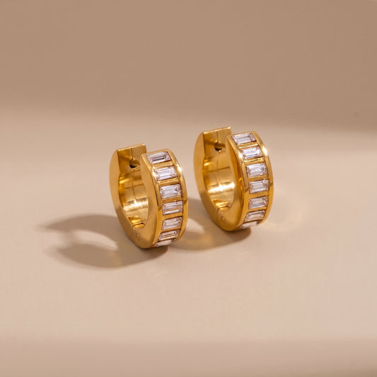 High quality Verona Gold Hoops featuring channel-set baguette crystals resting on a warm beige surface in natural sunlight.