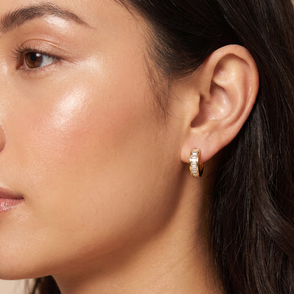 Close-up portrait of a woman wearing the waterproof Verona gold baguette crystal huggie hoop earring on her earlobe.
