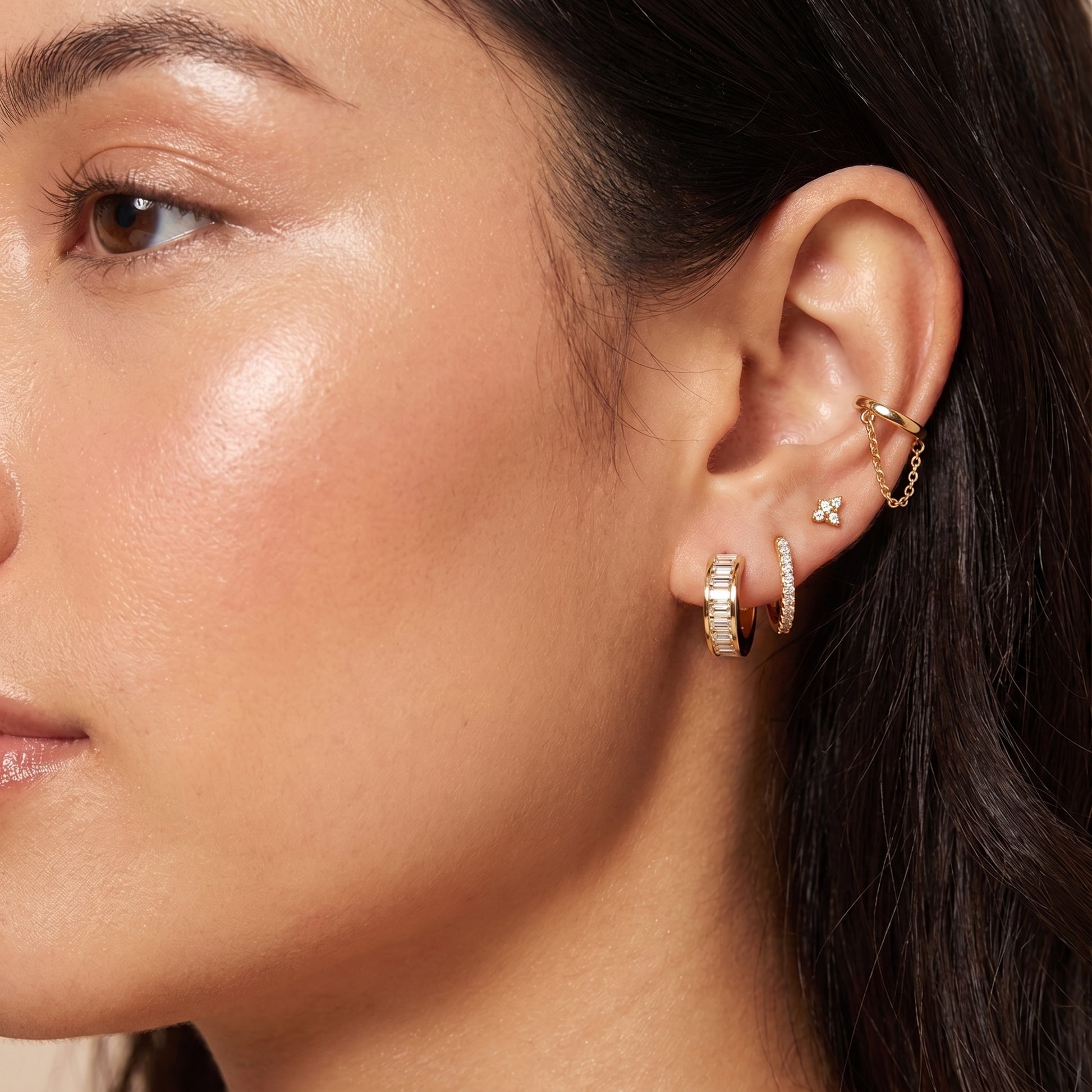 Modern gold ear stack on a woman featuring the skin friendly Verona baguette crystal huggie paired with a pavé hoop and chain cuff.