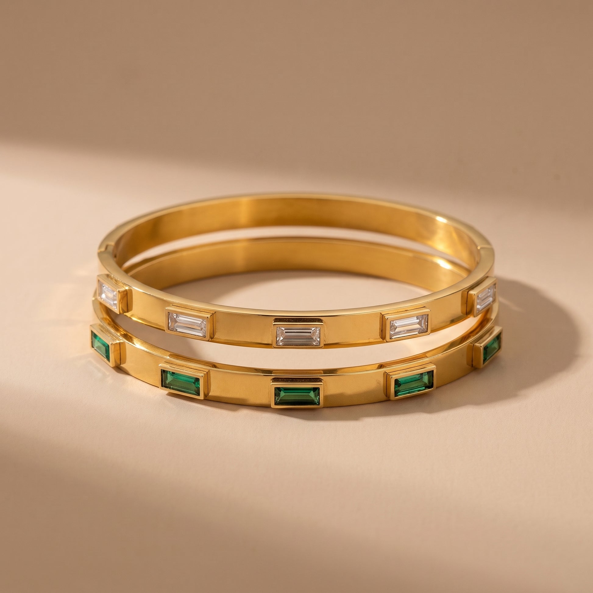 High quality Verona Gold Bracelets by Floravisha featuring raised bezel-set clear baguette crystals resting on a warm beige travertine surface under natural sunlight.
