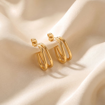 Tarnish-free Vienne gold double-band oval hoop earrings with stud post backings resting on draped champagne silk fabric.