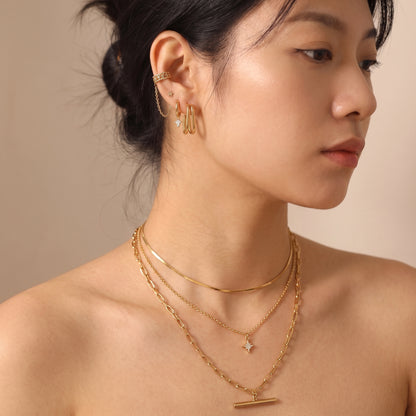 Skin friendly Vienne gold double oval hoops worn on a model's earlobe paired with a layered gold necklace stack in warm natural lighting.