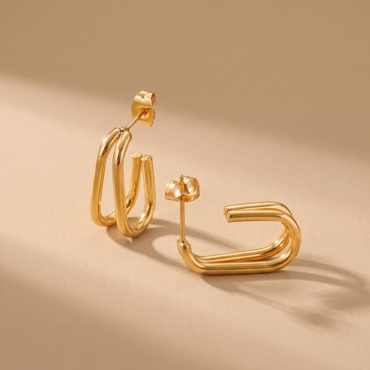 Waterproof Vienne gold double parallel oval hoop earrings displaying stud post and butterfly backings on a smooth beige surface.